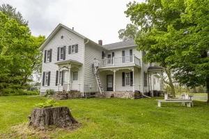 Two painters on a ladder and balcony painting the white siding of a two-story farmhouse